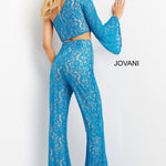 A woman modeling a bright blue lace two-piece outfit with a long-sleeve crop top and matching high-waisted flared pants, shown against a plain white wall. The brand name JOVANI appears on the right side.