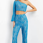 A woman modeling a bright blue lace two-piece outfit consisting of a one-shoulder long-sleeve crop top and matching high-waisted flared pants, photographed against a plain white studio background.