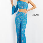 A woman models a bright blue lace two-piece outfit consisting of a one-shoulder crop top with long flared sleeves and matching high-waisted flared pants. The brand name 'JOVANI' is printed on the right side of the image against a plain white studio background.