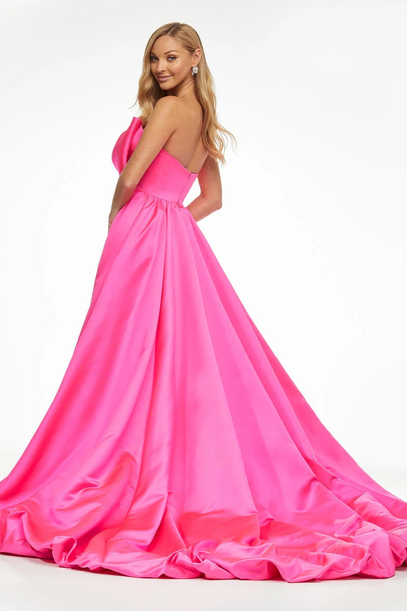 A woman modeling a bright hot pink one-shoulder ball gown with a voluminous skirt and train, photographed against a clean white studio background.