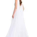 A woman modeling a white bridal gown from the back, featuring a sheer draped cape-style back drape, a beaded open back, and a long flowing tulle train against a plain white studio background.
