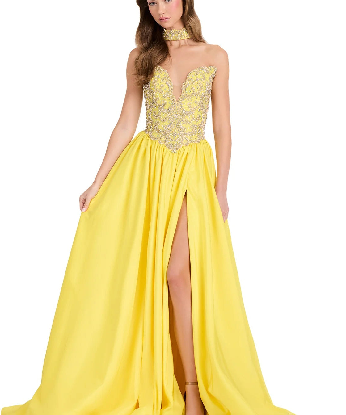 A woman modeling a bright yellow formal gown with a sheer lace bodice, choker neckline, and a thigh slit, photographed against a plain white studio background.