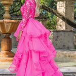Woman in a pink formal gown standing outdoors with a fountain and trees in the background