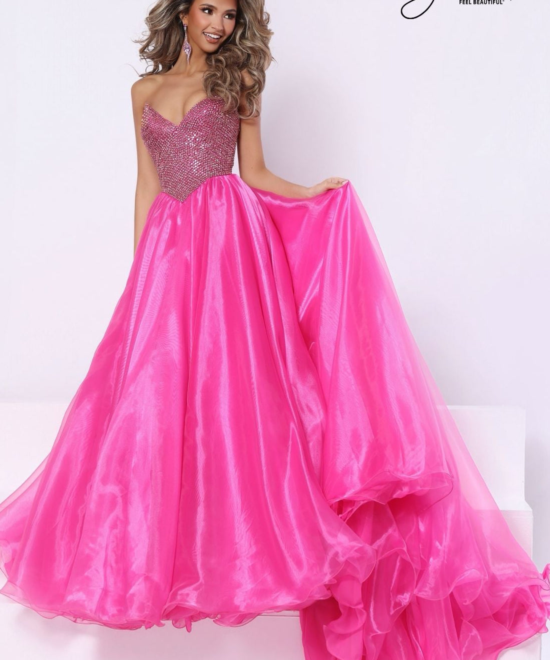 A woman modeling a bright pink formal gown with a full beaded sweetheart bodice and a full layered organza skirt, posed against a white studio background with a visible 'Johnathan Kayne' signature in the top right.