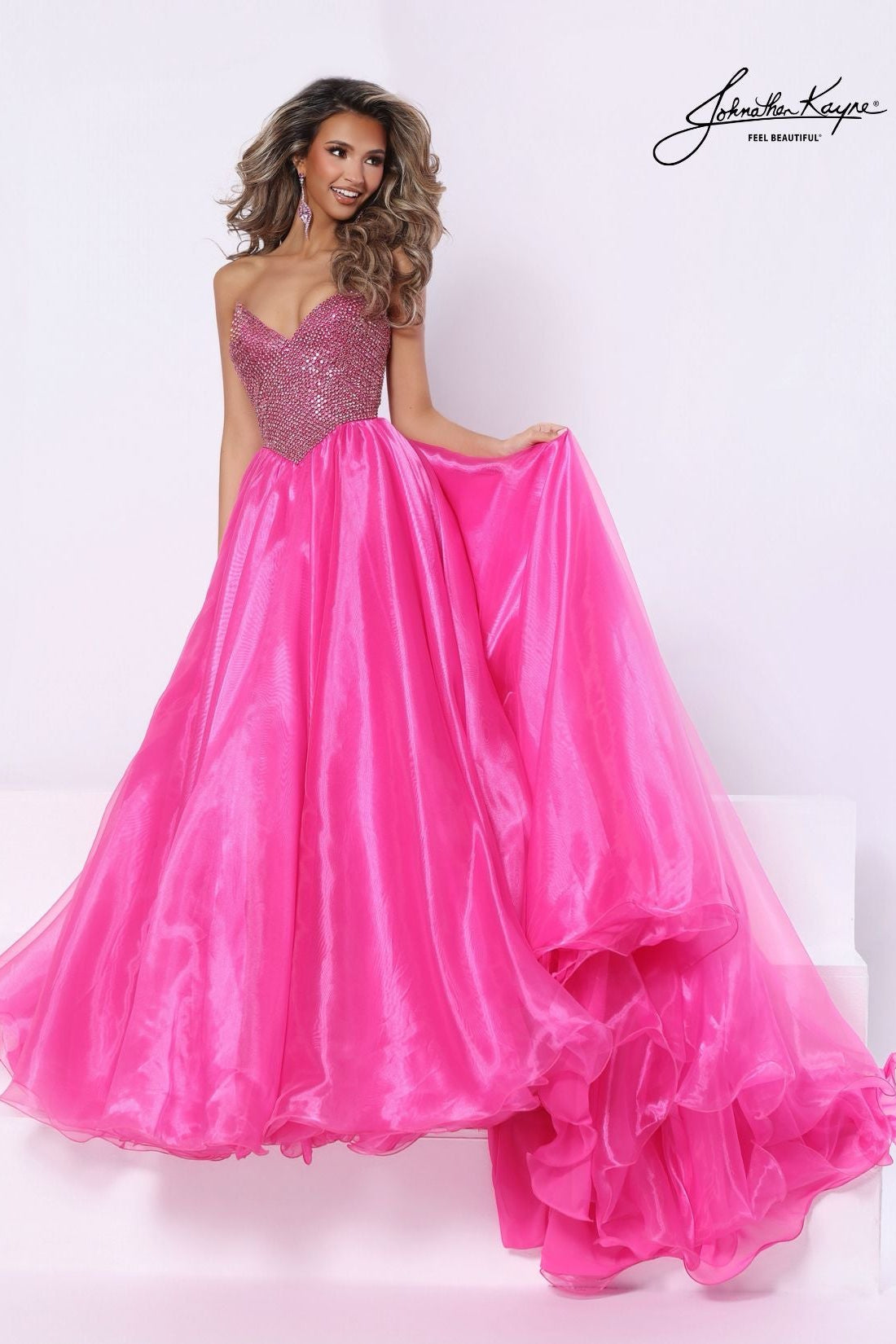 A woman modeling a bright pink formal gown with a full beaded sweetheart bodice and a full layered organza skirt, posed against a white studio background with a visible 'Johnathan Kayne' signature in the top right.