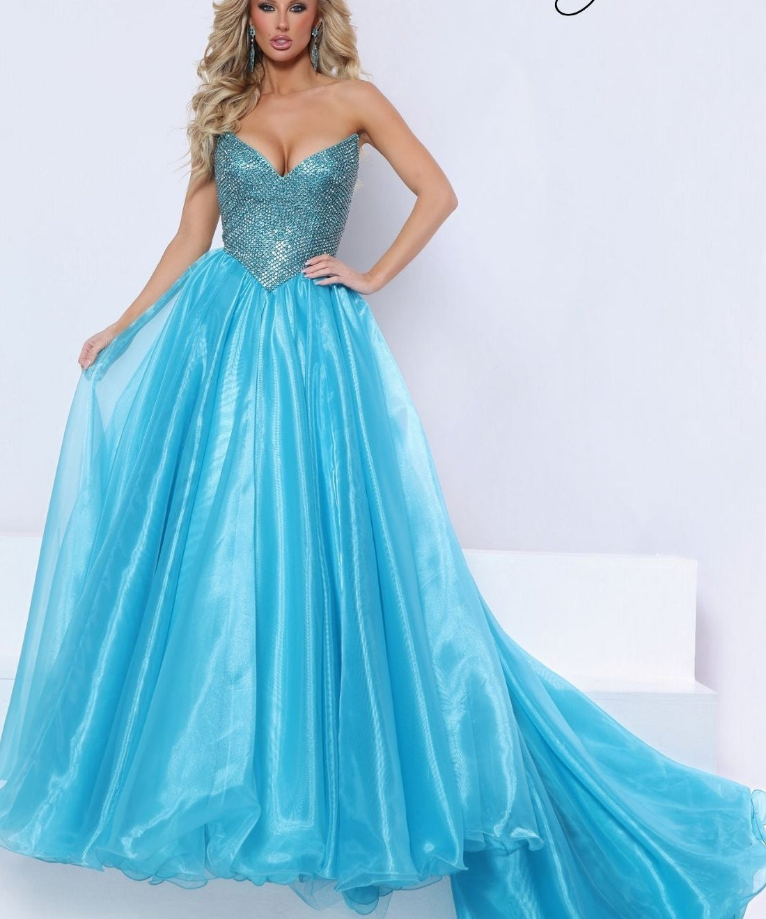 A woman models a strapless turquoise blue ball gown with a heavily embellished sequined sweetheart bodice and a full flowing skirt, photographed in a bright studio setting. The brand signature 'Johnathan Kayne' is visible in the top right corner.