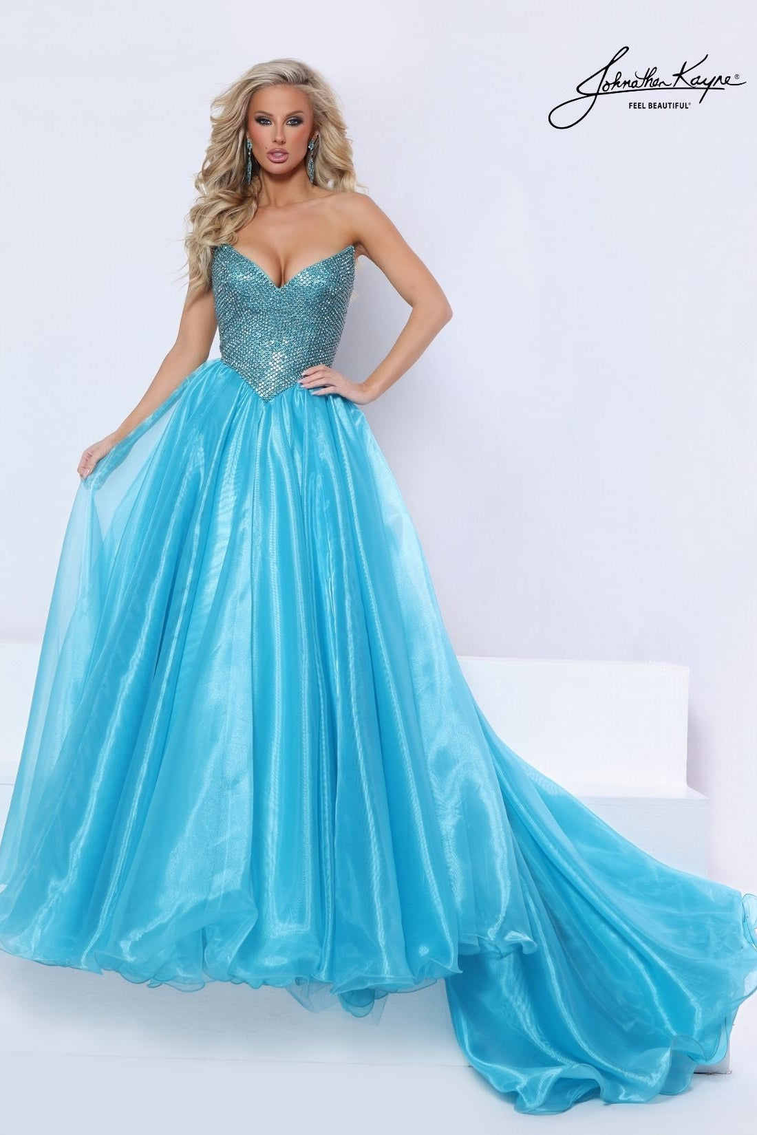A woman models a strapless turquoise blue ball gown with a heavily embellished sequined sweetheart bodice and a full flowing skirt, photographed in a bright studio setting. The brand signature 'Johnathan Kayne' is visible in the top right corner.