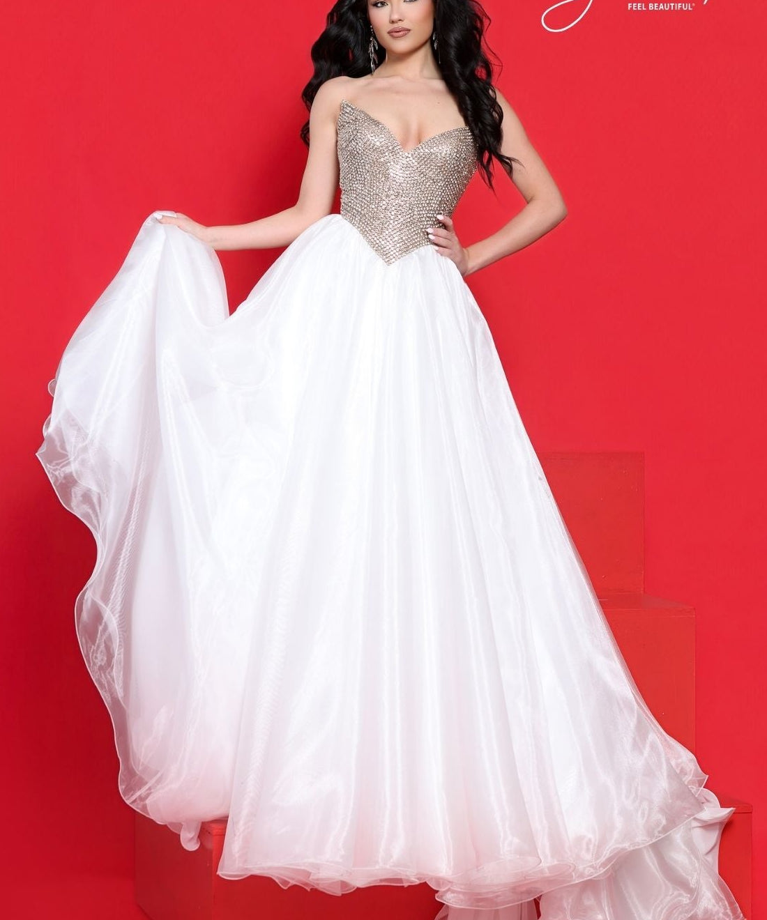 A woman models a strapless ball gown with a sparkling gold-beaded sweetheart bodice and a voluminous white organza skirt, posed against a solid red studio backdrop with a red block base.