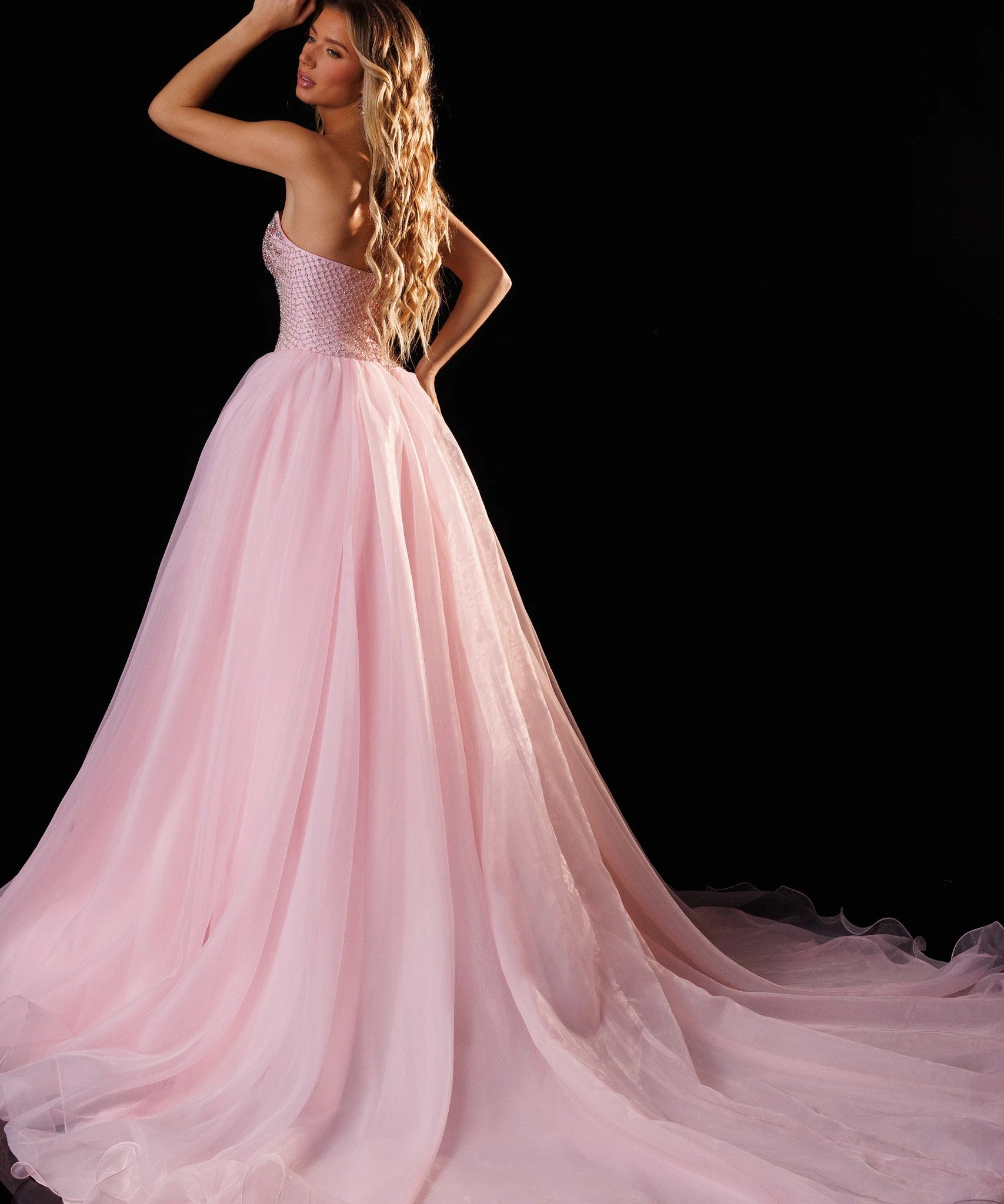 A woman modeling a pale pink strapless ball gown with a full tulle skirt and long train against a black studio background. The brand name 'RACHEL ALLAN' appears in the top right corner.