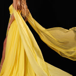 A woman modeling a flowing yellow evening gown with a long sheer train against a black background. The brand name 'RACHEL ALLAN' appears in the top right corner.