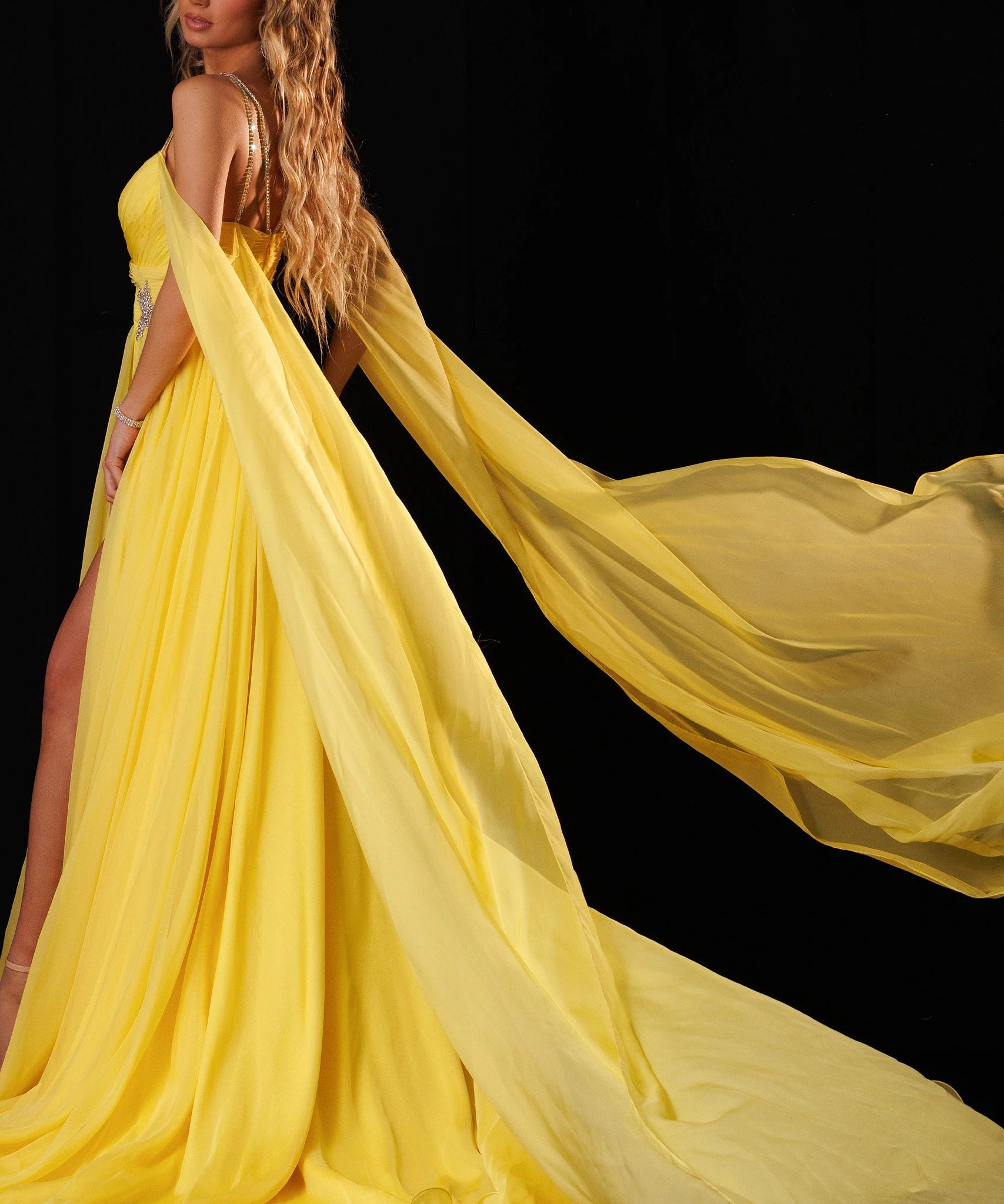 A woman modeling a flowing yellow evening gown with a long sheer train against a black background. The brand name 'RACHEL ALLAN' appears in the top right corner.