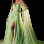 A model wears a Rachel Allan light green off-the-shoulder evening gown with a high leg slit and a flowing sheer cape, set against a solid black background.