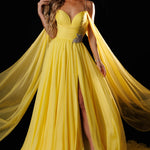 A woman models a bright yellow formal gown with a sweetheart neckline, thin straps, a high thigh slit, and a flowing sheer cape train against a black background. The brand name 'RACHEL ALLAN' is printed in the top right corner.