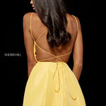 A woman shown from the back wearing a bright yellow spaghetti-strap dress with an open back and tie detail, photographed against a solid black background. The Sherri Hill brand name is visible on the left side.