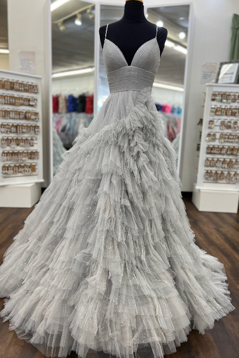 A voluminous white ball gown with a sweetheart neckline and a heavily ruffled, tiered tulle skirt, displayed on a black mannequin in a bridal boutique.