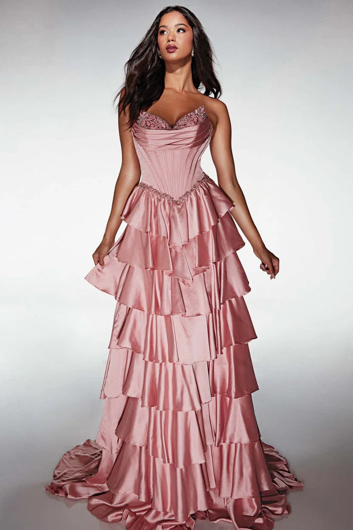 A woman modeling a strapless formal gown with a structured corset-style bodice and a full, tiered satin skirt in a dusty pink color, set against a light gray studio background.