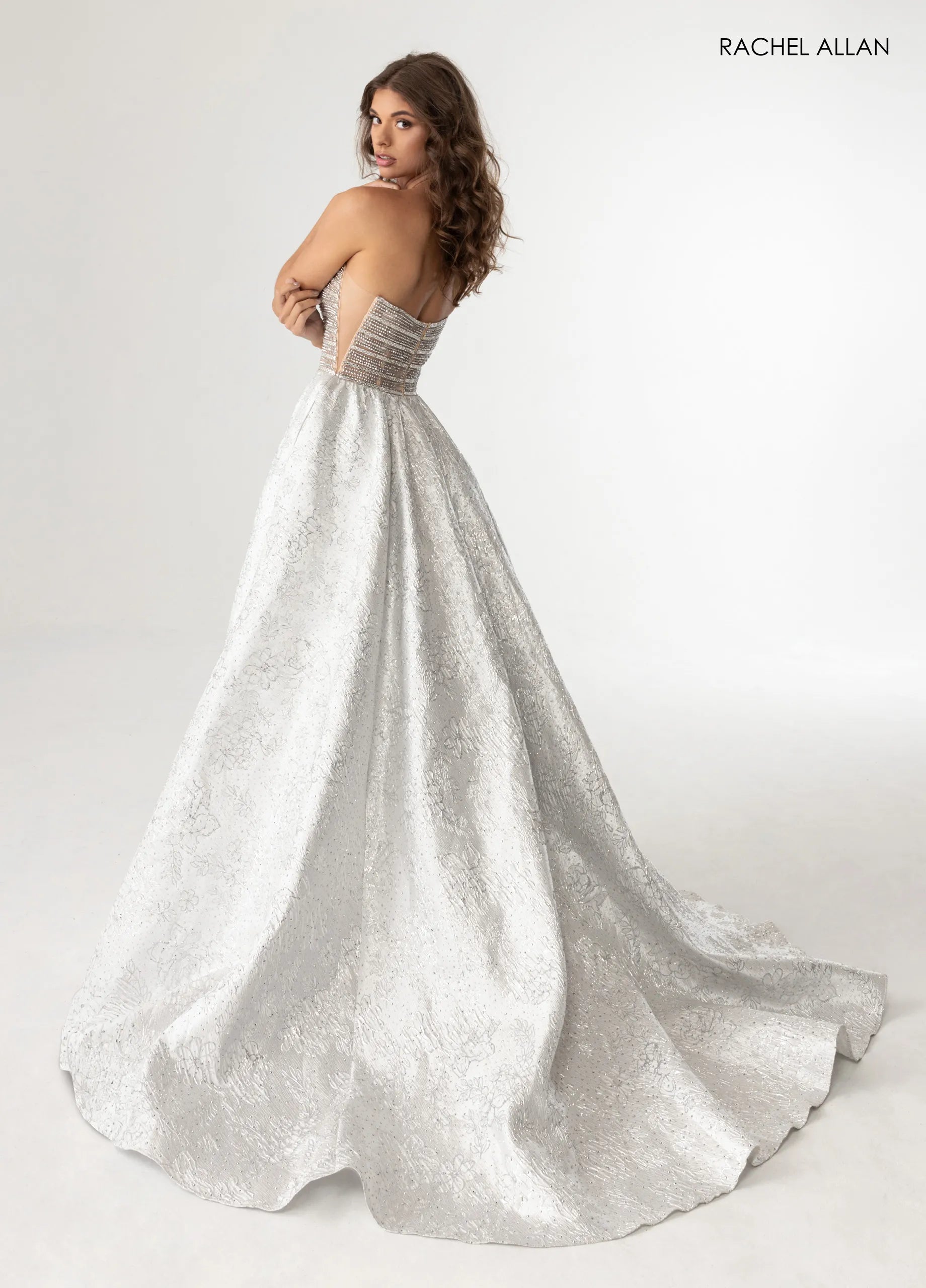 A woman modeling a strapless A-line wedding gown with a textured silver-white lace skirt and a sheer beaded waistband, photographed against a clean white studio background. The brand name 'RACHEL ALLAN' is printed in the top right corner.