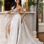 A woman models a strapless white lace ball gown with a sweetheart neckline, sheer corset-style bodice, high leg slit, and a long train in an elegant indoor room with a fireplace and mirror.