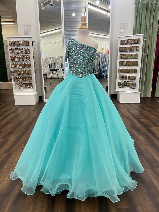 A voluminous ball gown dress displayed on a mannequin in a retail store. The dress features a one-shoulder neckline with a heavily beaded, embellished turquoise-blue bodice and a flowing, sheer tulle skirt in a light aqua/mint color.