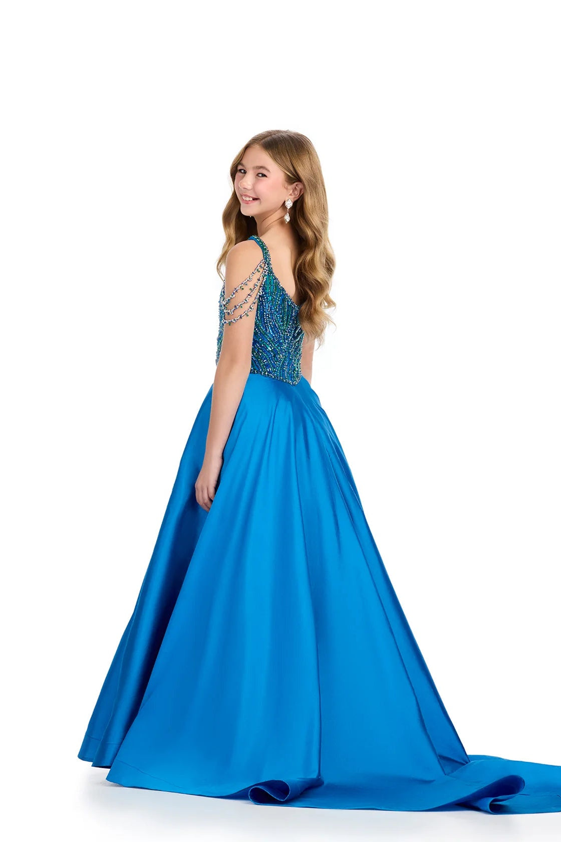 A young woman modeling a bright blue ball gown with a beaded, embellished back bodice and a long satin train, photographed against a solid white background.