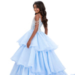 A young girl modeling a light blue quinceañera dress with a beaded bodice and a full, tiered tulle skirt, photographed against a solid white background.