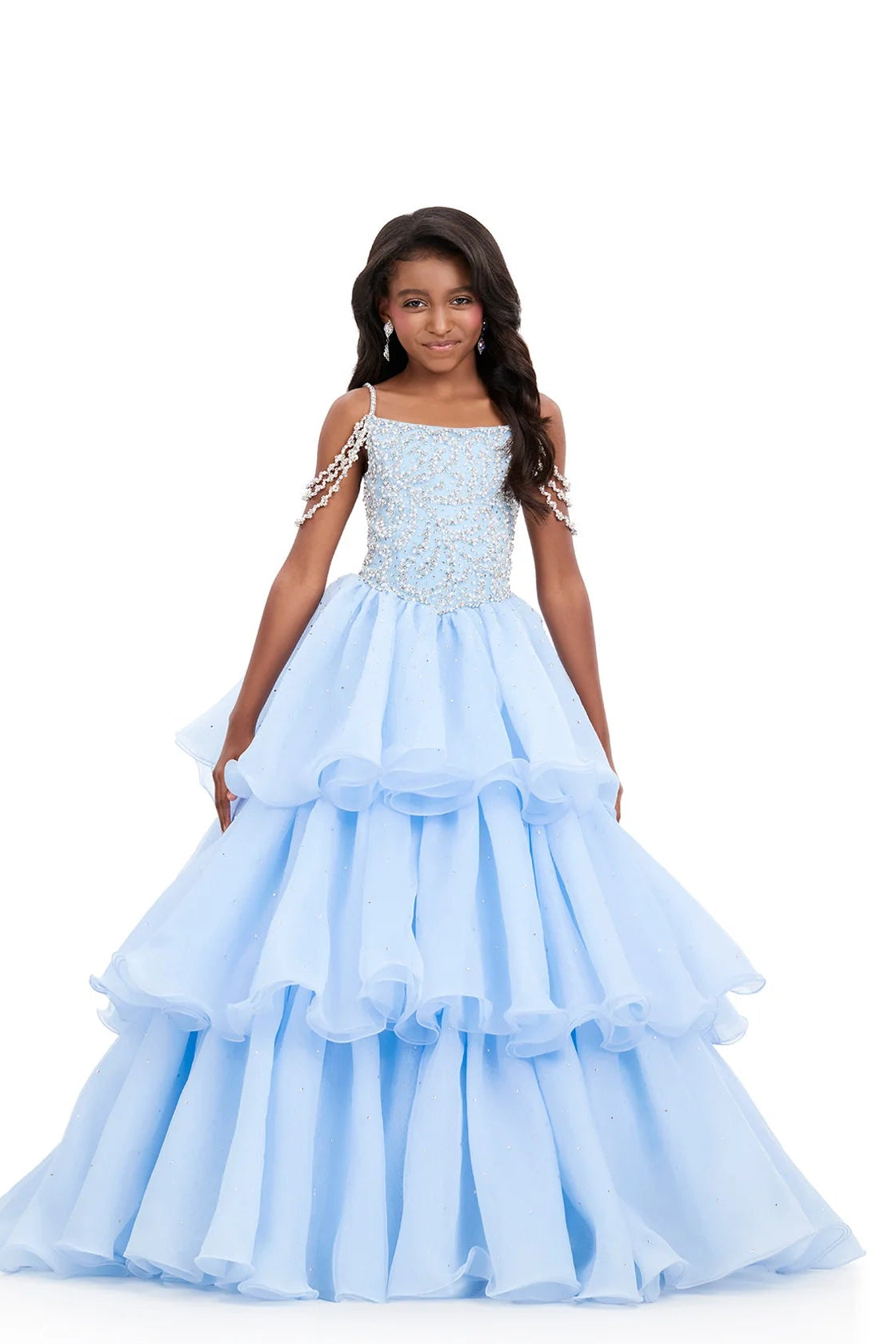 Young girl wearing a light blue formal gown with ruffled layers on a white background