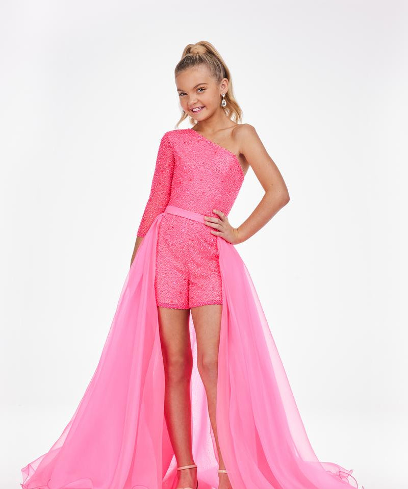 Young girl is modeling a pink organza overskirt atop a pink romper on a white background.