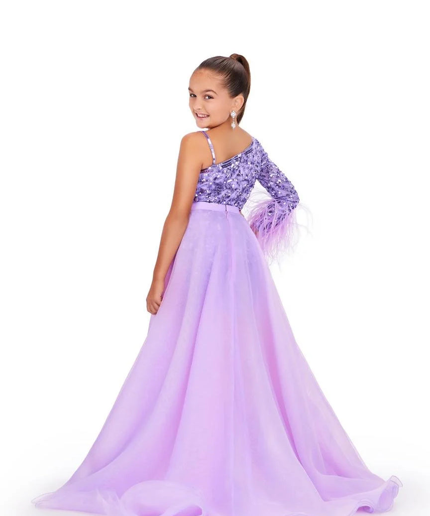 Young girl wearing a purple one-shoulder romper with an orchid overskirt on a white background.