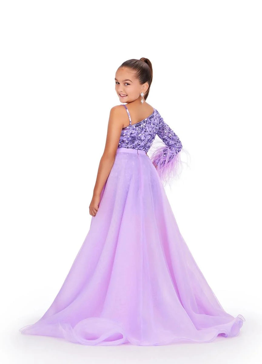 Young girl wearing a purple one-shoulder romper with an orchid overskirt on a white background.