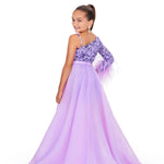 Young girl wearing a purple one-shoulder romper with an orchid overskirt on a white background.