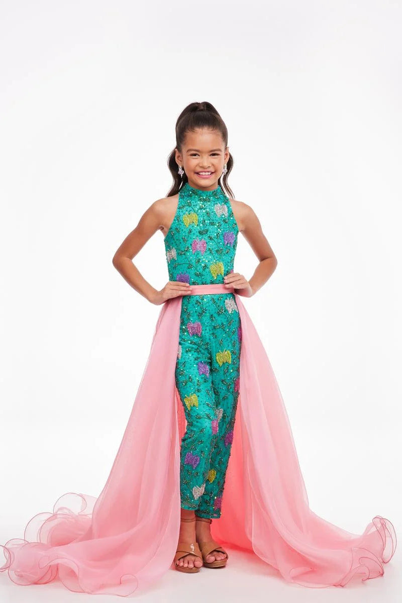 A young girl models a pink organza overskirt atop a green floral jumpsuit.