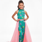 A young girl models a pink organza overskirt atop a green floral jumpsuit.