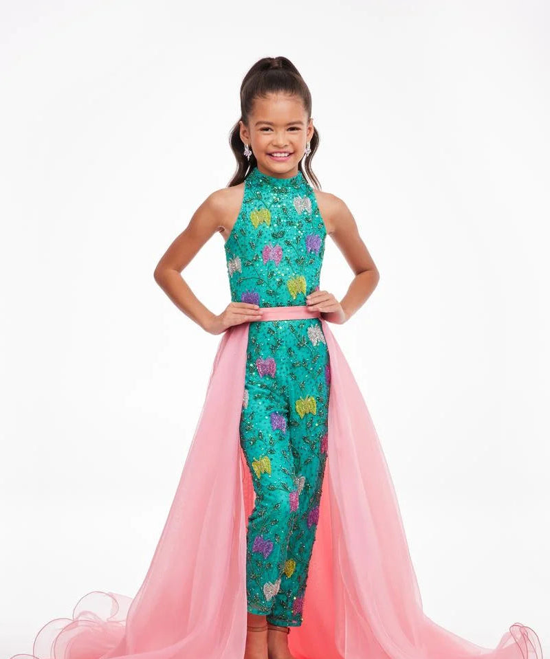 A young girl models a pink organza overskirt atop a green floral jumpsuit.