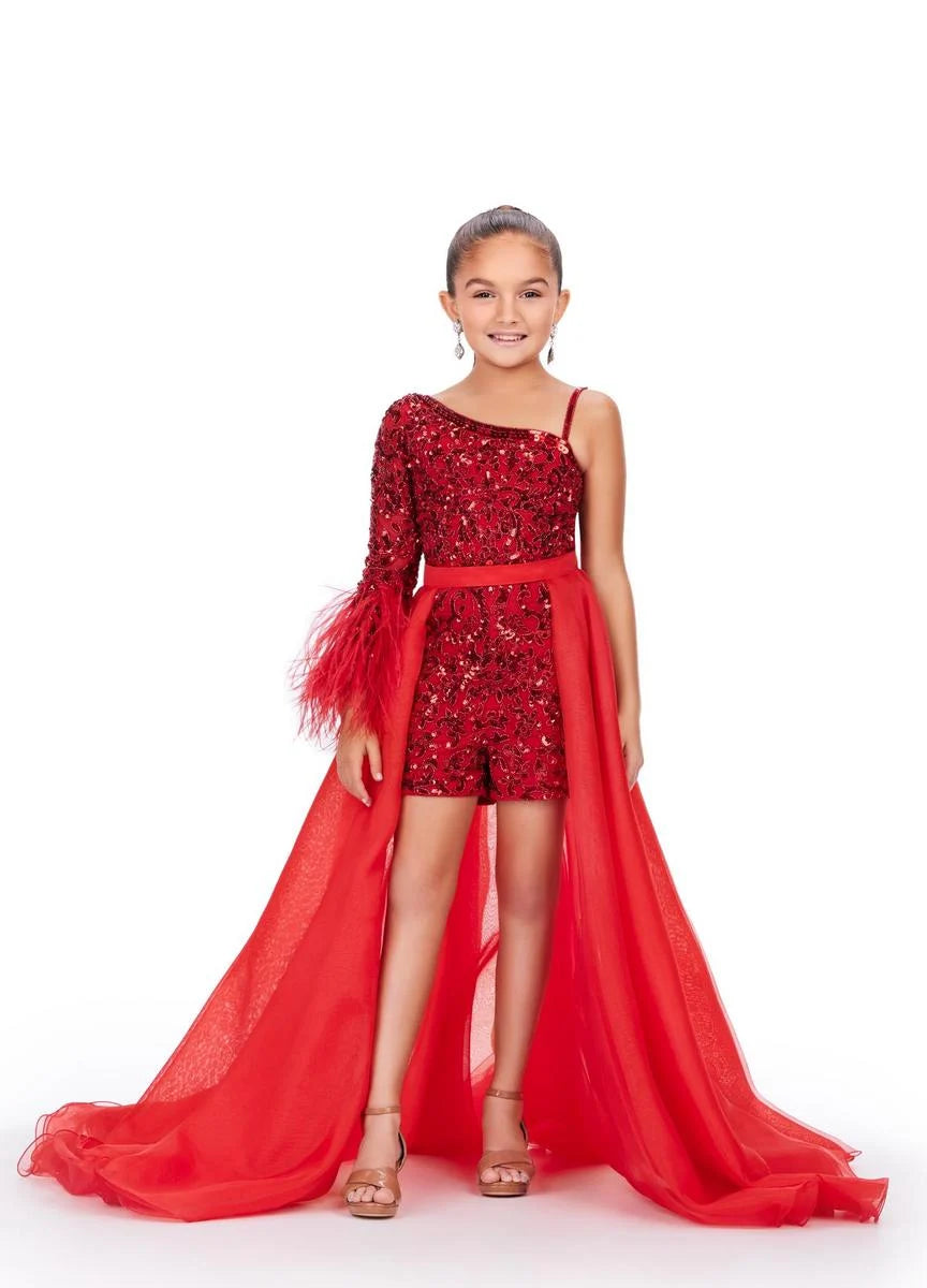 A young girl models a red organza overskirt atop a one shoulder beaded romper in front of a white background.