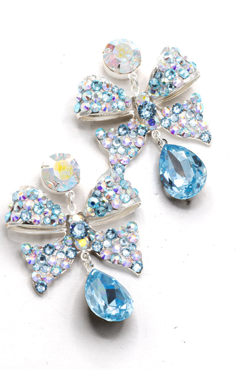 A pair of silver-tone drop earrings featuring a bow-shaped design and clusters of iridescent rhinestones, with light blue teardrop crystals, shown on a plain white background.