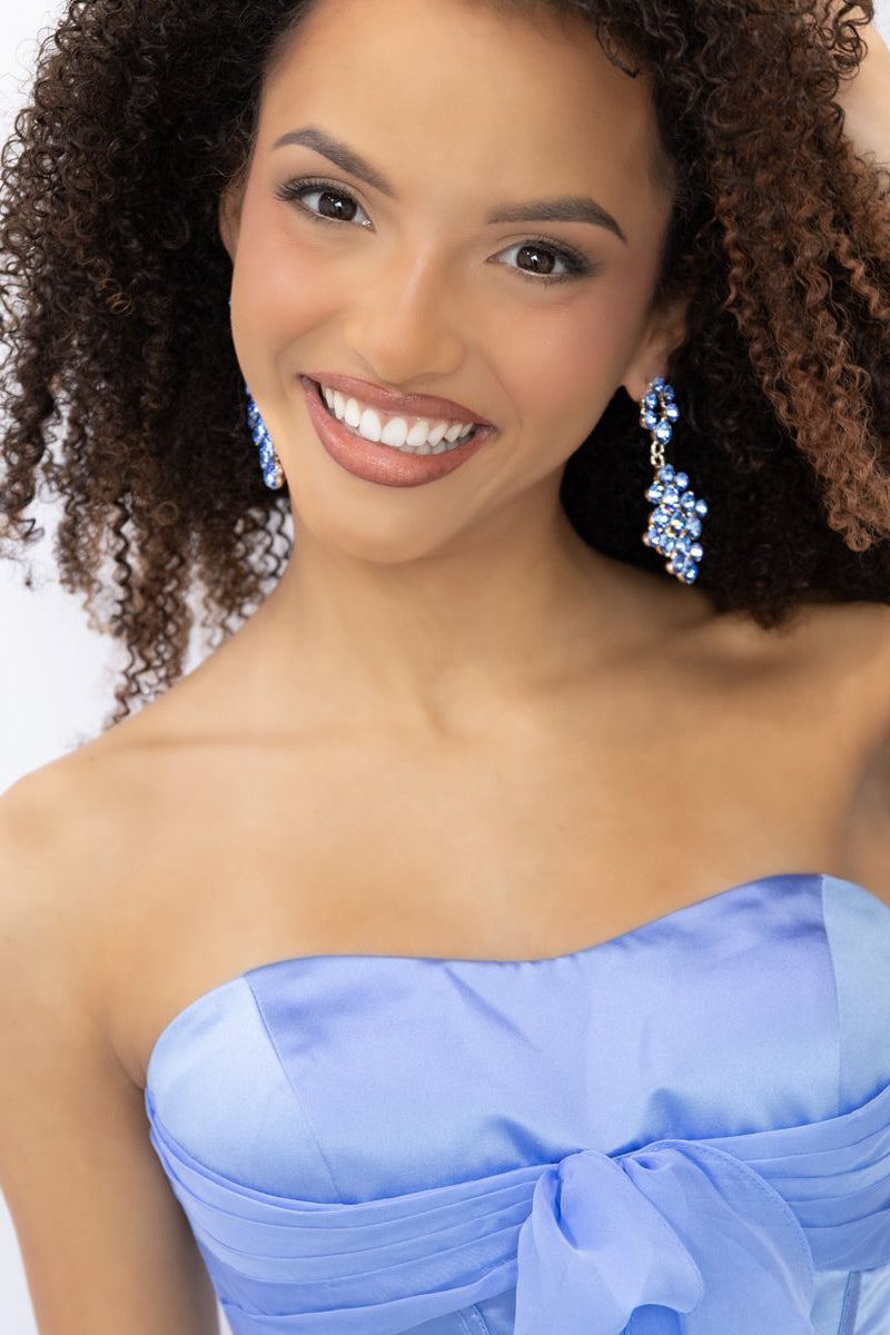 A woman wearing a strapless light blue formal gown with a large bow at the bust a flowing skirt, and matching light blue earrings. 