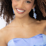 A woman wearing a strapless light blue formal gown with a large bow at the bust a flowing skirt, and matching light blue earrings. 