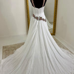 A white gown displayed on a black mannequin in front of a mirror, featuring a fitted bodice with floral embroidery at the waist and a long flowing train.