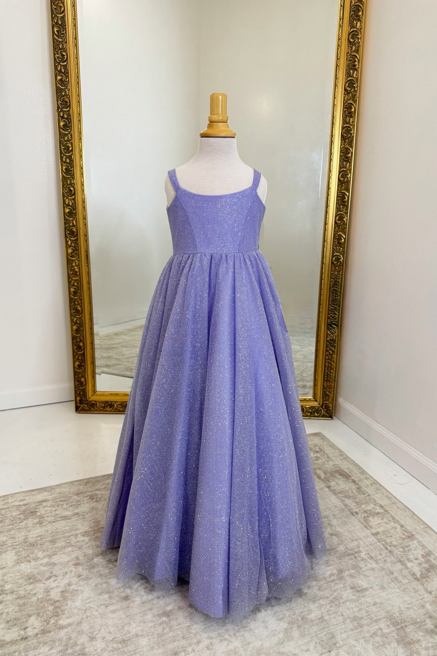 A lavender purple sleeveless A-line dress with a textured bodice and a full tulle skirt, displayed on a mannequin in front of a large gold-framed mirror.