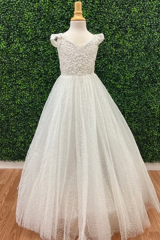 White tulle ball gown dress with a lace bodice and cap sleeves, displayed on a mannequin in front of a green hedge wall and wood floor.