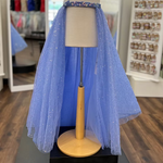 A periwinkle tulle overskirt displayed on a mannequin torso stand in a retail store. The garment has a sparkly blue sequin waistband and a layered tulle skirt with small reflective glitter-like dots.