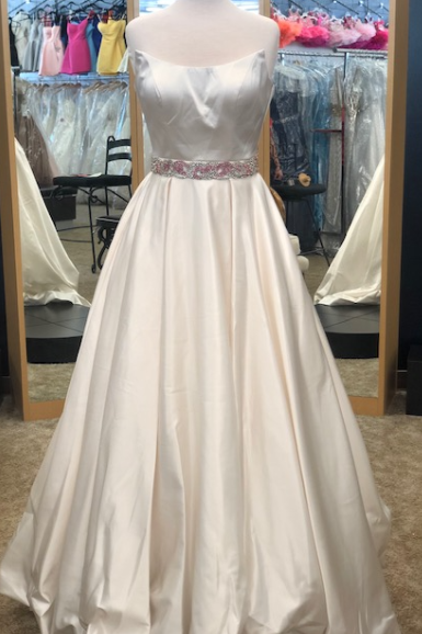 An ivory satin A-line ball gown with a sweetheart neckline and a sparkling embellished waistband, displayed on a mannequin in a bridal boutique.