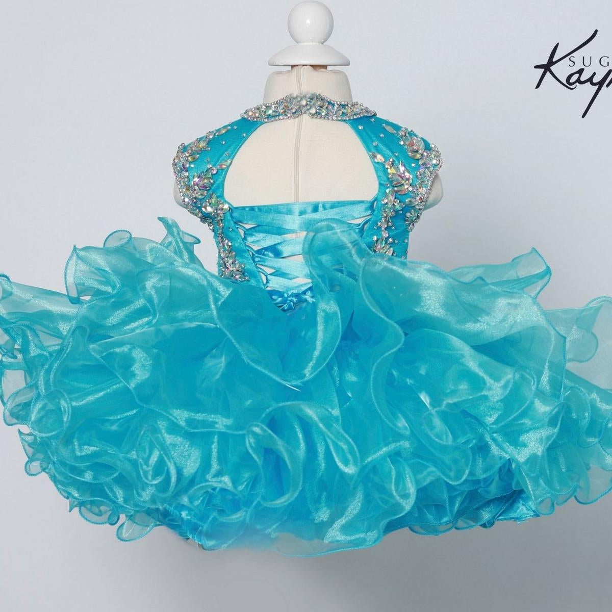 Turquoise dress with ruffled skirt on a mannequin against a light gray background, featuring the brand 'Sugar Kaye'.