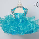 Turquoise dress with ruffled skirt on a mannequin against a light gray background, featuring the brand 'Sugar Kaye'.